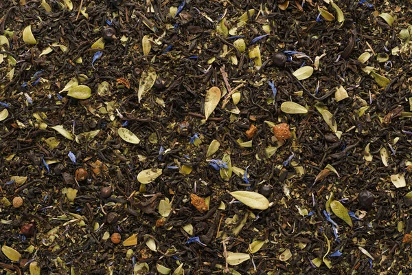 Dry black tea mixed with herbs and berries as a background.