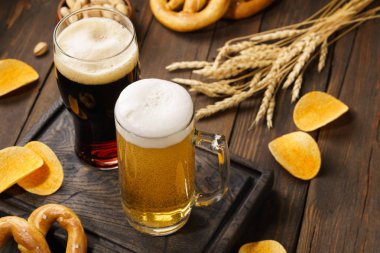 Ahşap arka planda çeşitli atıştırmalıklarla açık ve koyu bira.