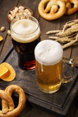 Ahşap arka planda çeşitli atıştırmalıklarla açık ve koyu bira.