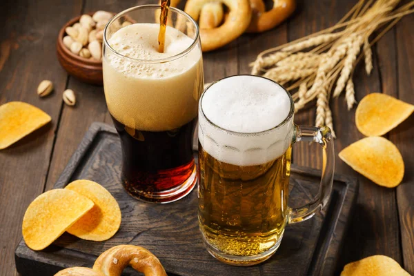Ljust och mörkt öl med olika tilltugg på en träbakgrund. — Stockfoto