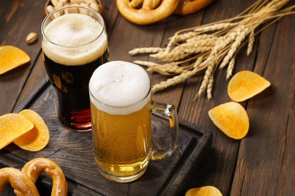 Ahşap arka planda çeşitli atıştırmalıklarla açık ve koyu bira.