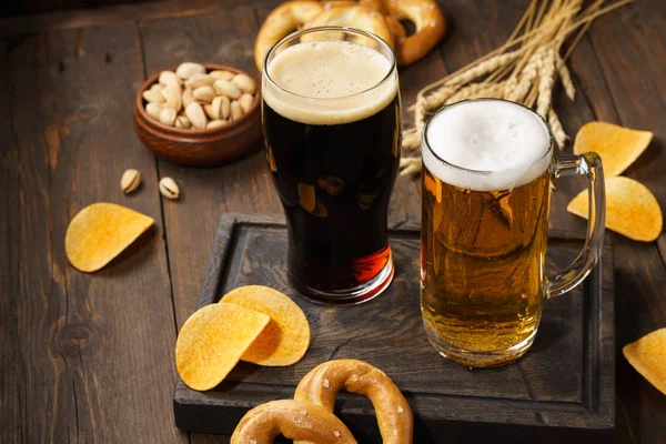 Light and dark beer with various snacks on a wooden background.