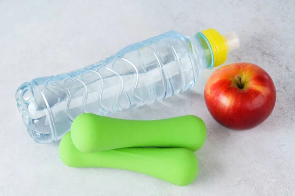 Bottle of water, dumbbells and apple on light gray background. — Stock Photo, Image