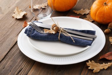 Yapraklar ve balkabaklarıyla sonbahar sehpası. Tahta bir masada beyaz tabaklar ve süslü çatal bıçak takımı..