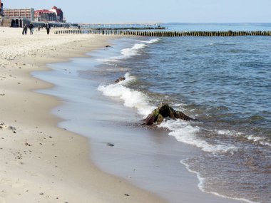 Terk edilmiş deniz kıyısı, beyaz kum, soğuk mavi gökyüzü, parlak güneşli bir gün, küçük bir tatil köyü, uzakta nadir görülen insan siluetleri. Baltık Denizi.