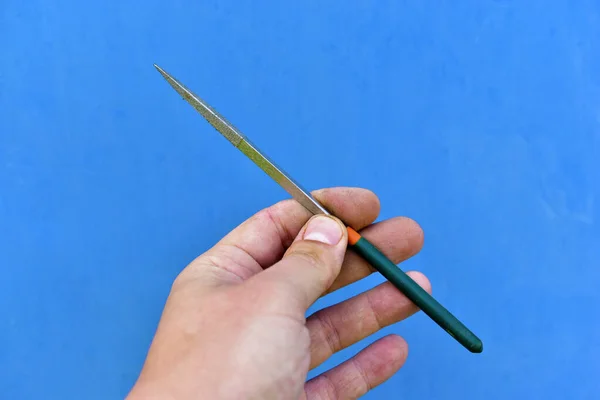 Small tool file in hand on a blue background