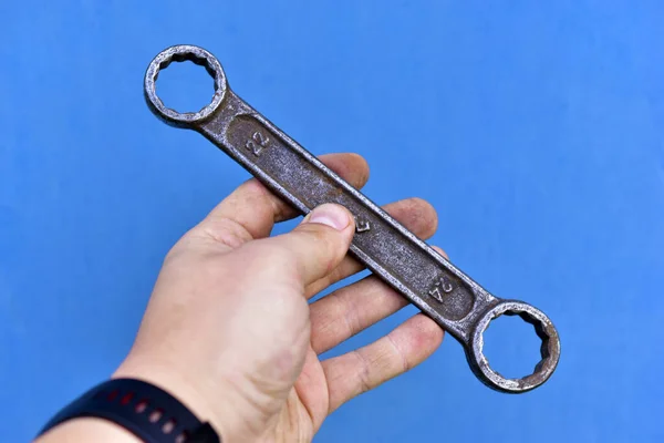 Rusty iron cap wrench in hand on a blue background