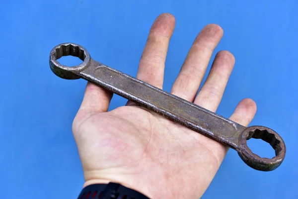 Rusty iron cap wrench in hand on a blue background