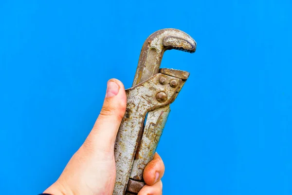 Iron gas wrench in hand on a blue background