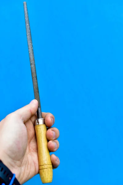 Iron round file with wooden handle in hand on blue background