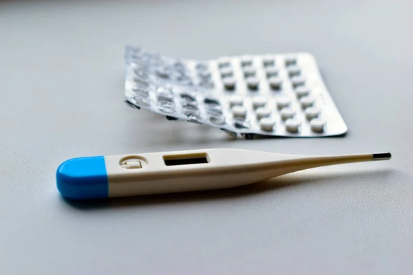 Electronic thermometer and blister with tablets on a white background