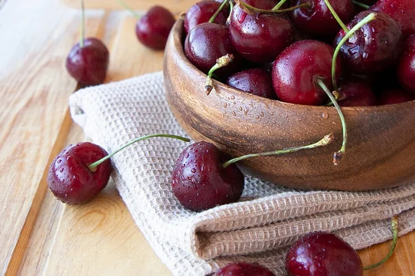 Ahşap zemin üzerinde kahverengi bir havluyla ahşap bir tabakta olgun kırmızı kirazlar.