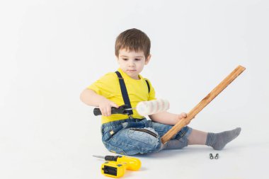 İnşaatçı kıyafetli küçük bir çocuk beyaz arka planda tamirat yapıyor.