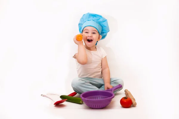 A little boy in a chef\'s hat cooks in a toy kitchen  on a white background