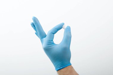 Tıbbi lateks ya da lastik eldiven mavi ya da mavi. Tablet, ilaç, vitamin beyaz arka planda izole edilmiş erkek elinde.