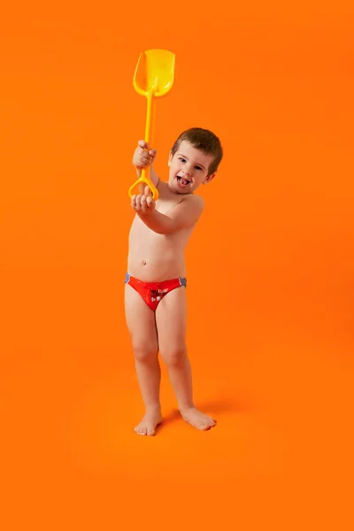 Smiling Boy Red Bathing Shorts Yellow Toy Shovel Orange Background — Stock Photo, Image