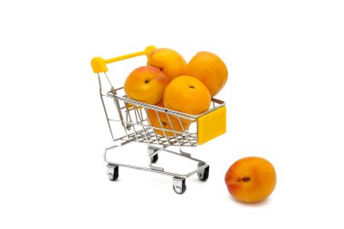 Küçük bir alışveriş arabasında sarı kayısılar ya da beyaz arka planda sepet