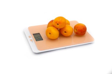 Beyaz arka planda, mutfak terazisinde sarı kayısılar. Tartma konsepti