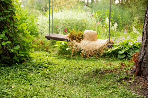 Salıncakta saman şapka ve yeşil arka planda sarı çiçekler. Dinlenme konsepti