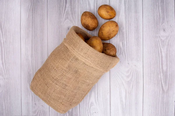 Nieuwe Aardappel Geïsoleerd Een Jute Zak Houten Ondergrond — Stockfoto