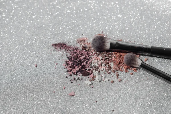 Maquiagem escovas com sombra esmagada colorida sobre o fundo de prata brilhante — Fotografia de Stock