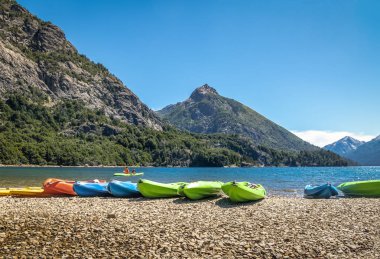 Colorful Kayaks in a lake surrounded by mountains at Bahia Lopez in Circuito Chico  - Bariloche, Patagonia, Argentina clipart