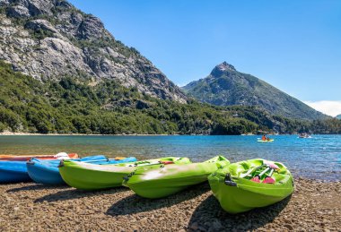 Colorful Kayaks in a lake surrounded by mountains at Bahia Lopez in Circuito Chico  - Bariloche, Patagonia, Argentina clipart