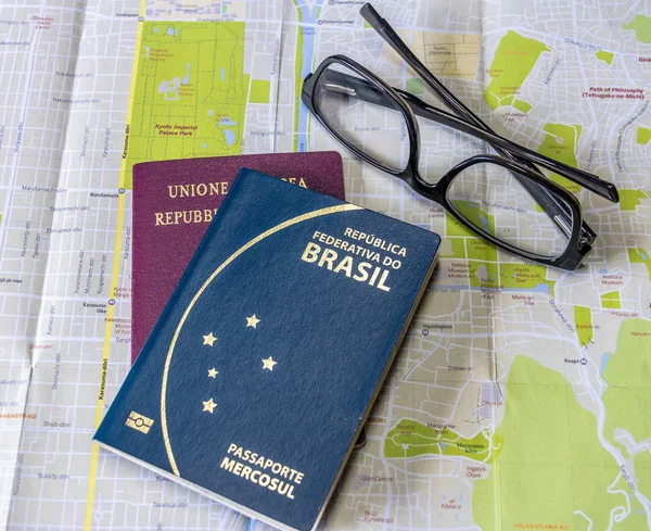 Planning a trip - Brazilian and Italian passports on city map with glasses