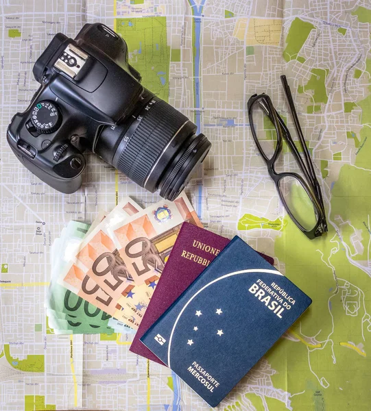 Planning a trip - Brazilian and Italian passports on city map with euro bills money, camera and glasses
