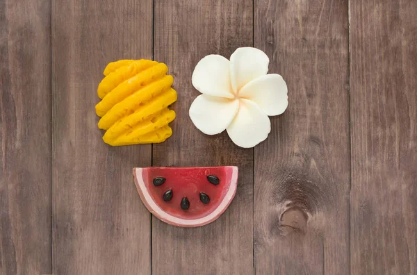 Hand made soap in the shape of fruit yellow pineapple, watermelon and flower on wooden background.