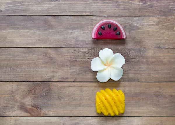 Hand made soap in the shape of fruit yellow pineapple, watermelon and flower on wooden background.