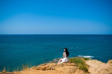 Uzun beyaz elbiseli, romantik, genç bir esmer kız adanın kenarında oturuyor. Güneydoğu Asya, Tayland 'da egzotik beyaz kumsal manzarası. Dağdan görünüm.