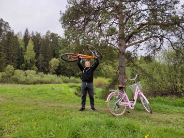 Ormandaki bir ormanda genç bir adam dinleniyor. Adam spor bisikletini kafasının üstüne kaldırdı. Kadın retro pembe bisiklet ayakta duruyor.