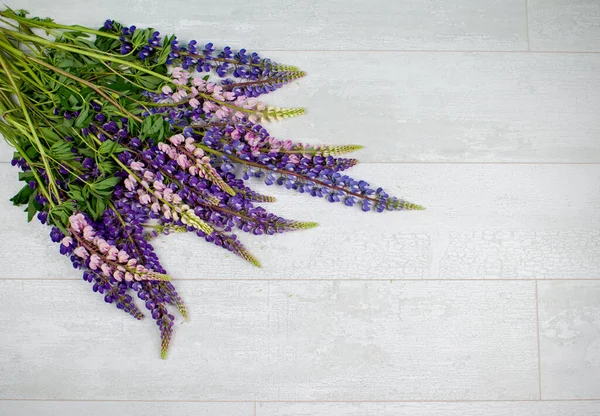 A bouquet of field flowers on a light grey wood background. Violet and pink lilac or lavender.