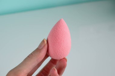 Pink beauty tear-shaped blender, clean egg-shaped sponge isolated on light background. Cosmetic tool for makeup in hand. clipart