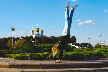 Bir kız ellerinin üzerinde baş aşağı şehir merkezinde bir kare üzerinde duruyor.