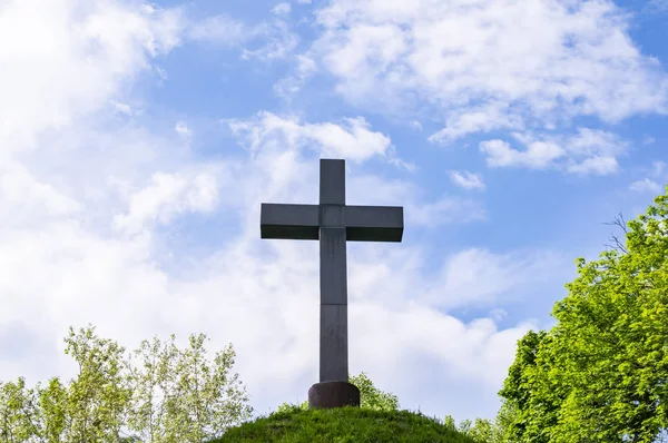 Christian cross on a green hill hill under a cloudy sky