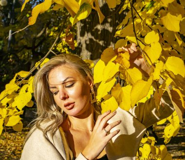 Sarı sonbahar yeşilliklerinin arka planında sarışın bir kız..