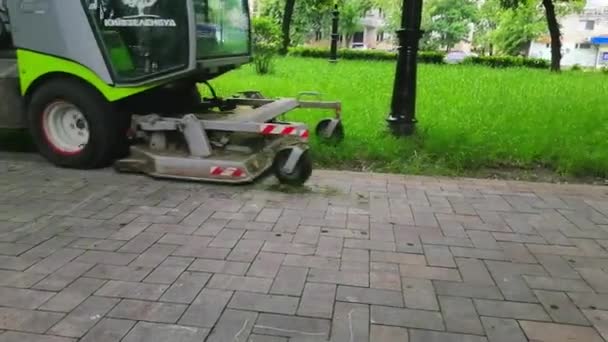 Un trattore falcia un prato di erba verde in un parco pubblico cittadino . — Video Stock