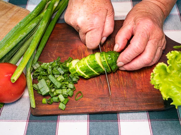 Cutting a vegetable a green cucumber with a knife on a cutting board. Green vegetable salad. Cook. Home kitchen. Vegetarian food. Recipe. Promotional photo. Hands of a man. Vitamins