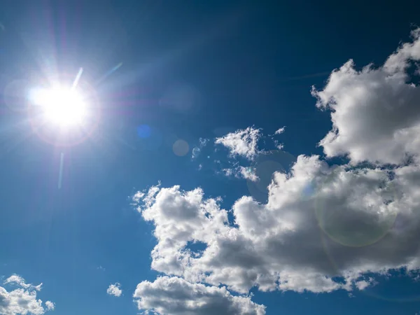 The sun on a background of blue sky with white clouds. Cloudy landscape. Nature. Space. Sunlight. Sun glare. Admire the view. Background image. Free space for text. Template. Poster.