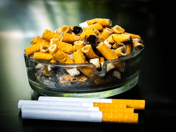 Glass ashtray with cigarette butts on a black background. Smoking cigarettes. Do not smoke. Harm to health. Background image. Place for text. Smoker\'s health. Passive smoking.