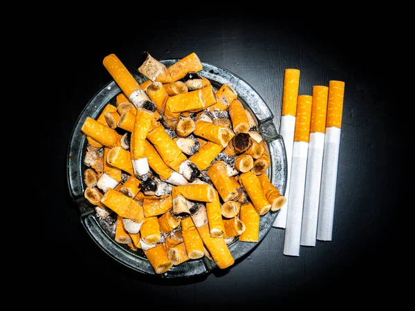Glass ashtray with cigarette butts on a black background. Smoking cigarettes. Do not smoke. Harm to health. Background image. Place for text. Smoker\'s health. Passive smoking.