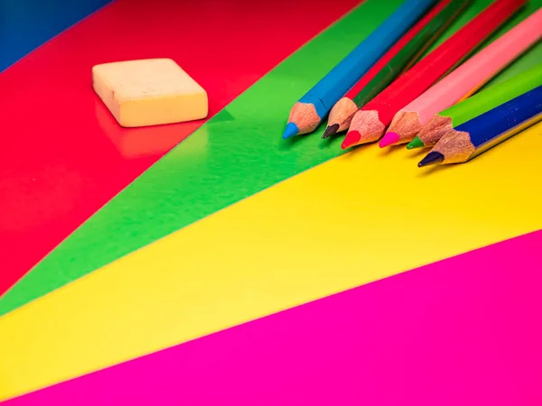 Colored pencils for drawing on the table. Multicolored background. Sharpened pencil. School drawing lesson. Eraser. Place for your text. Template. Background image. Poster. Sheets of colored paper.