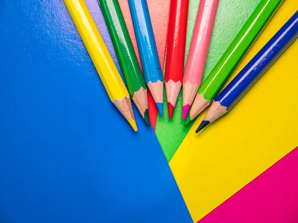 Colored pencils for drawing on the table. Multicolored background. Sharpened pencil. School drawing lesson. Eraser. Place for your text. Template. Background image. Poster. Sheets of colored paper.
