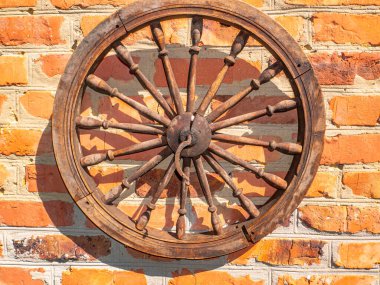 Duvardaki eski ahşap tekerlek. At arabasının ahşap tekerleği. Kırmızı tuğla duvar. Dekor elemanı. Retro tarzı. Arkaplan resmi. Metnin için yer.