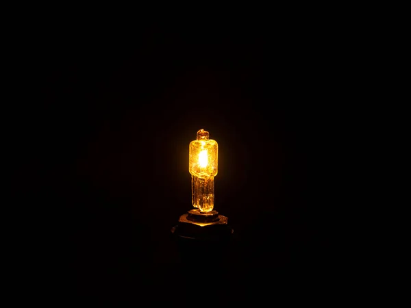 Glow of a halogen bulb in the dark. Light of an electric halogen bulb in the dark. Electric light source. Electric lighting. Electricity. Black background. Room lighting. Utility bills. Background.