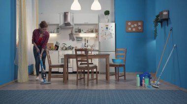 Ev hanımı mavi bir elektrik süpürgesi ile zemin temizler.