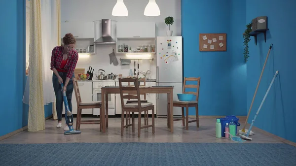 Dona de casa limpa o chão com um aspirador azul . — Fotografia de Stock