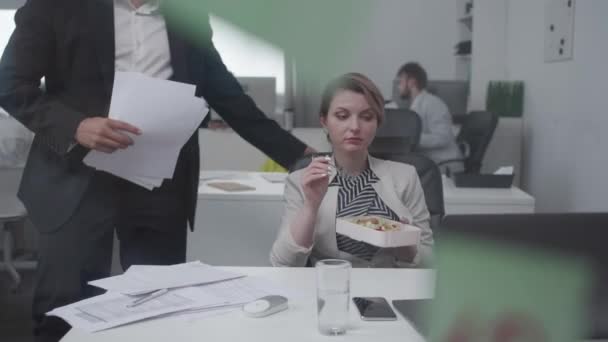 Une femme mange au bureau, un homme lui donne des documents . — Video